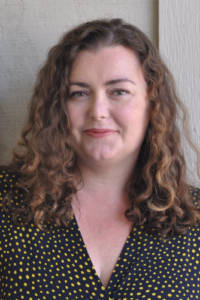 Professional Staff headshot. A woman with curly hair smiling at the camera.