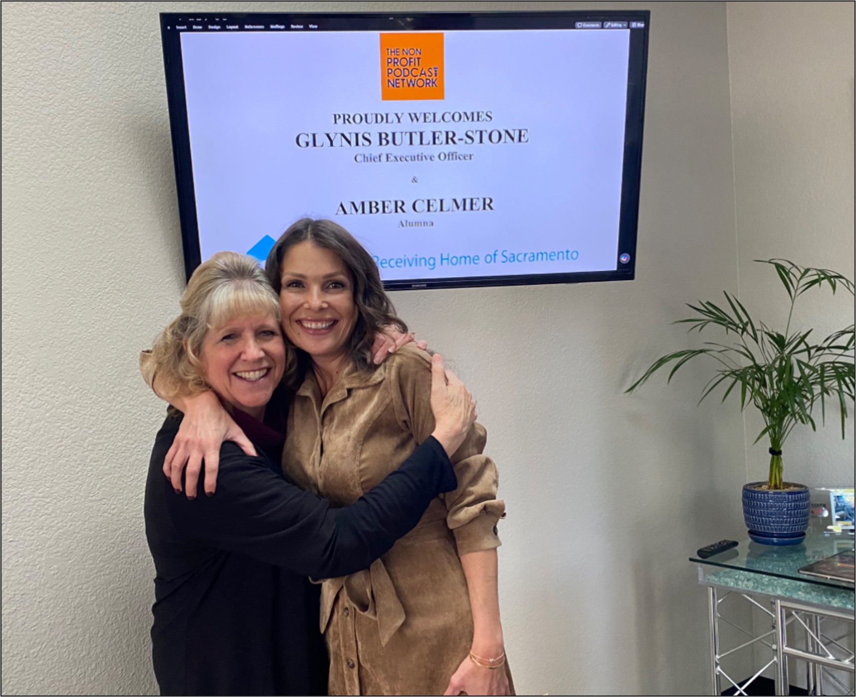 Two women embracing in front of a screen with their names displayed