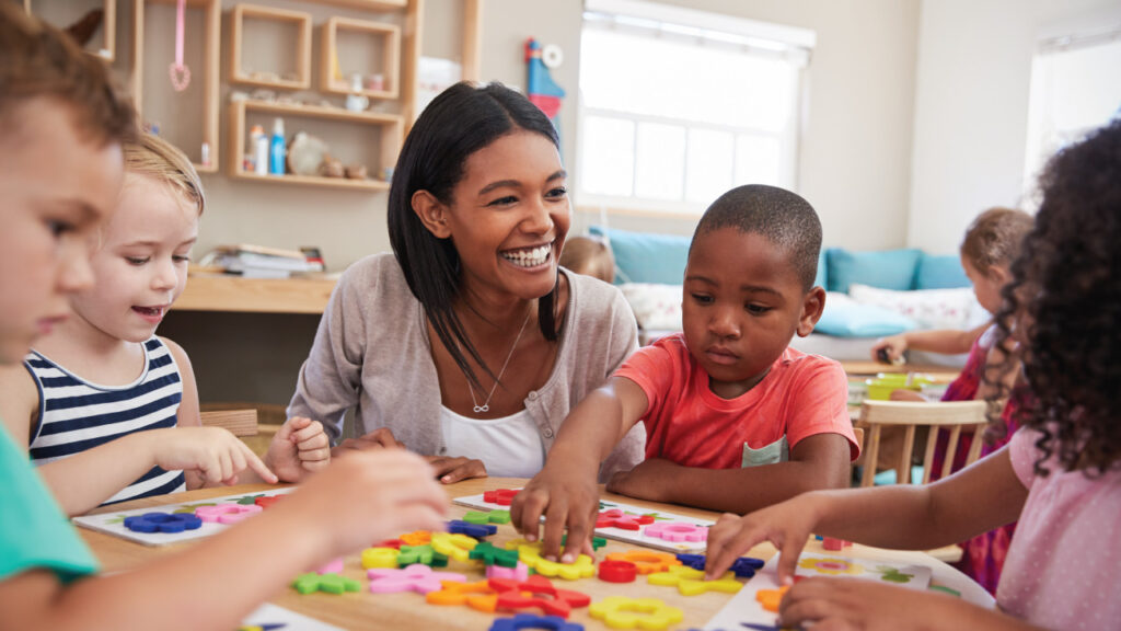 preschool teacher with her students gathered around a table playing and learning together