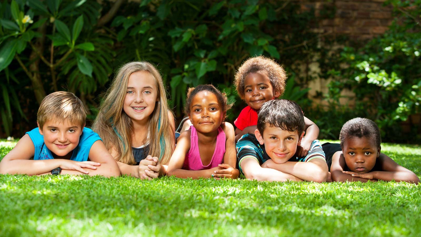 group of tweens laying on stomachs in grass smiling at camera